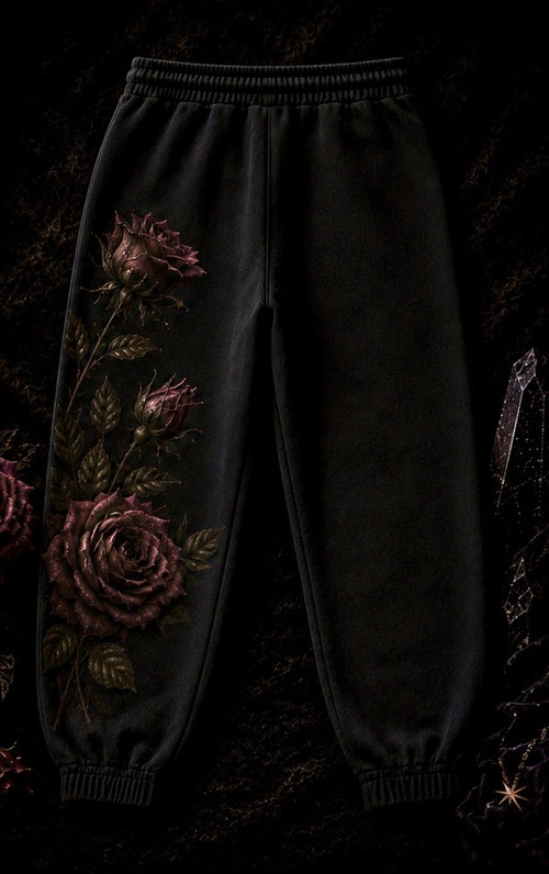 Black jogger sweatpants with a gothic rose graphic print on the left leg, displayed against a dark, textured background.